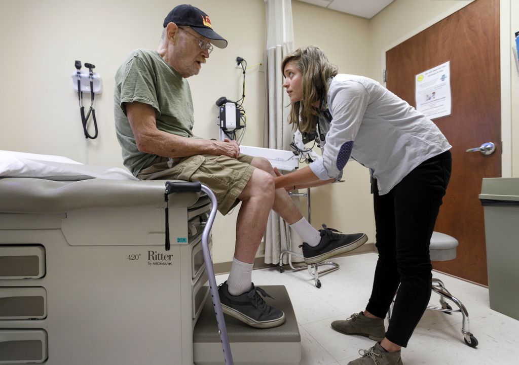 female doctor looking at the knee of an elderly man
