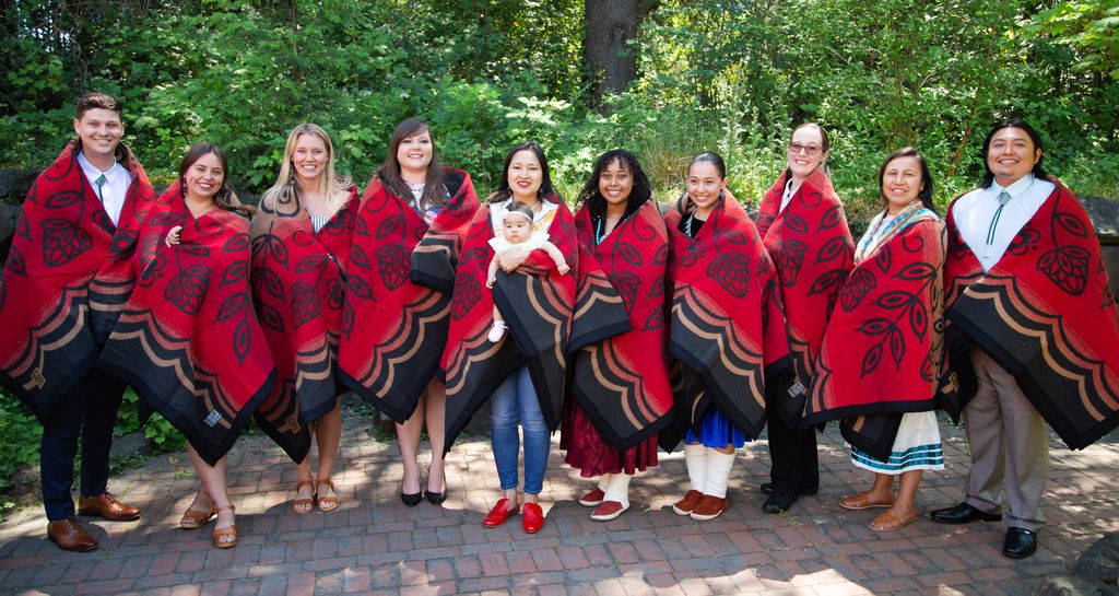 a group photo showing ten native american students lined up, with red blankets draped around their shoulders