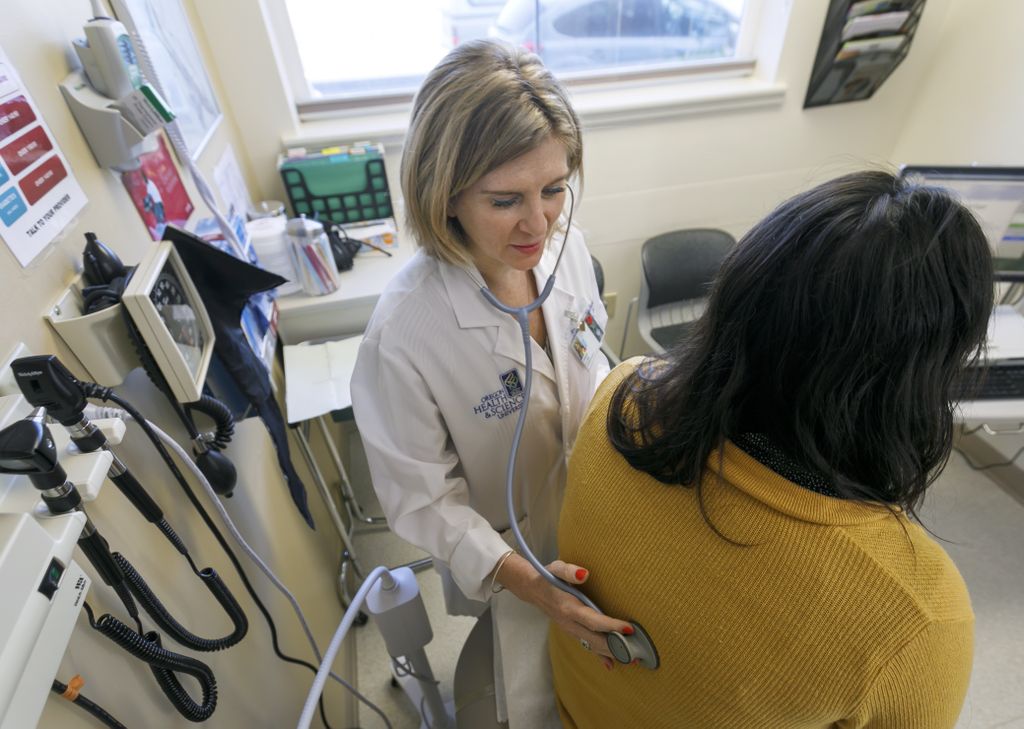 image of medical professional listening to a patient's lungs with a stethoscope in a doctor's office