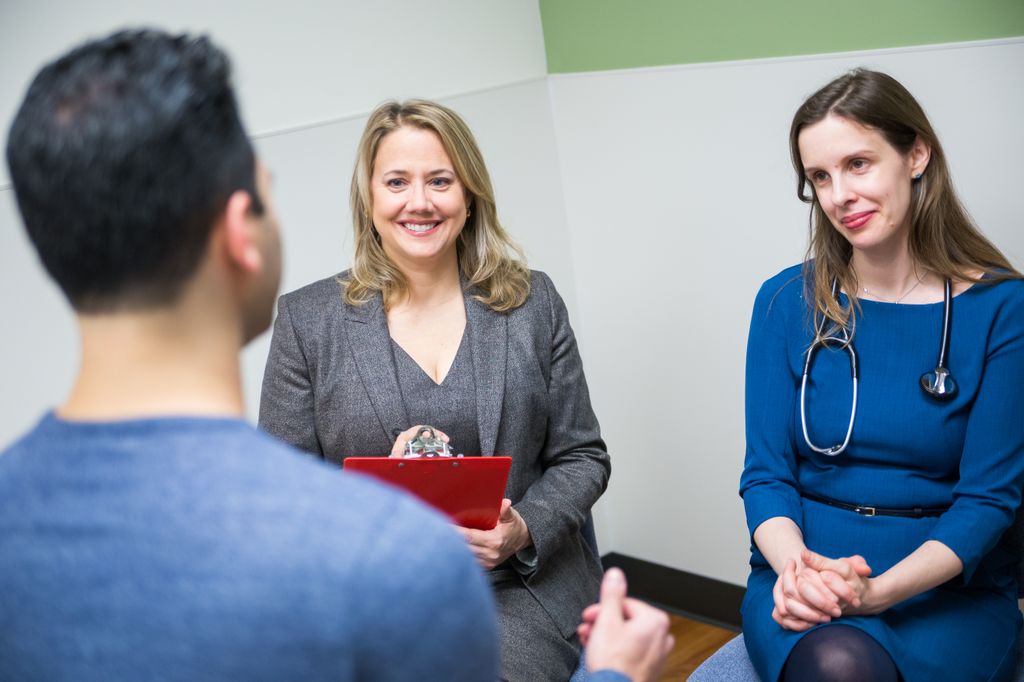 doctors kovacs and khan, smiling as they talk to a patient, seen from the back