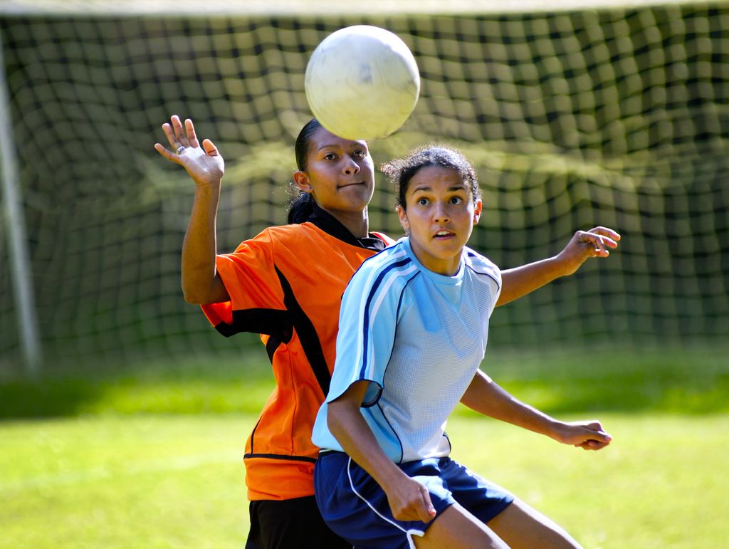 two teenage soccer players about to head a soccer ball