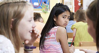 Unhappy Girl Being Gossiped About By School Friends In Classroom