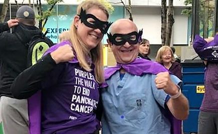 two people, woman and man, in masks and purple capes