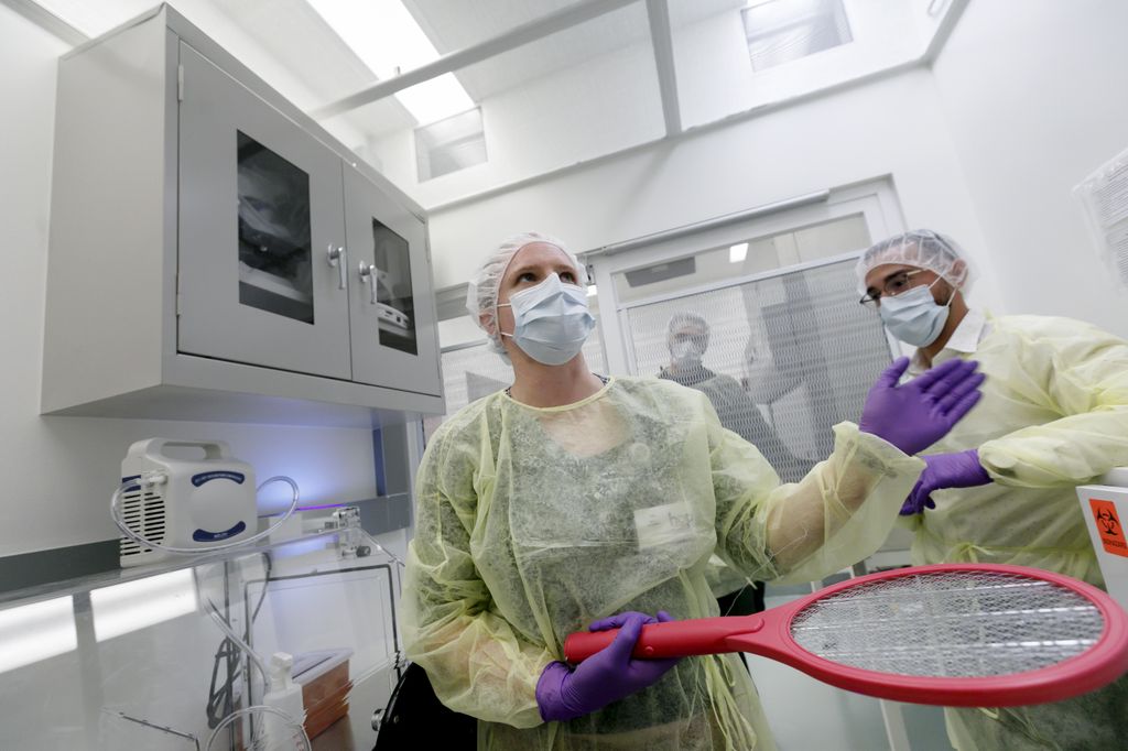 woman and man, fully clothed in protective clothing, in a small research room, holding an electrified tennis racket which is a bug zapper