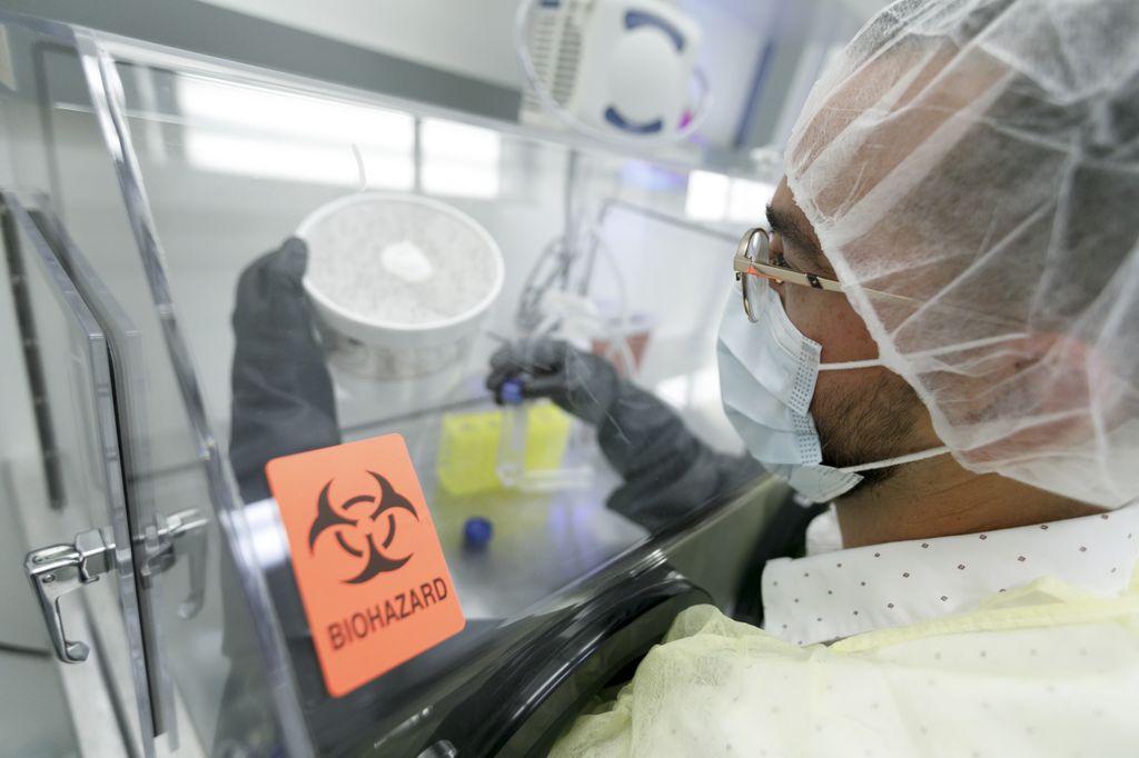 man with hands inside of a clear container, using an instrument to poke inside of a styrofoam container full of mosquitoes.
