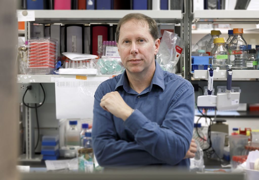 man wearing blue shirt, in a laboratory, with arms crossed, looking at camera