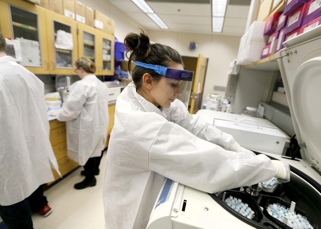 woman with face shield in white coat working in laboratory loading tubes into a machine