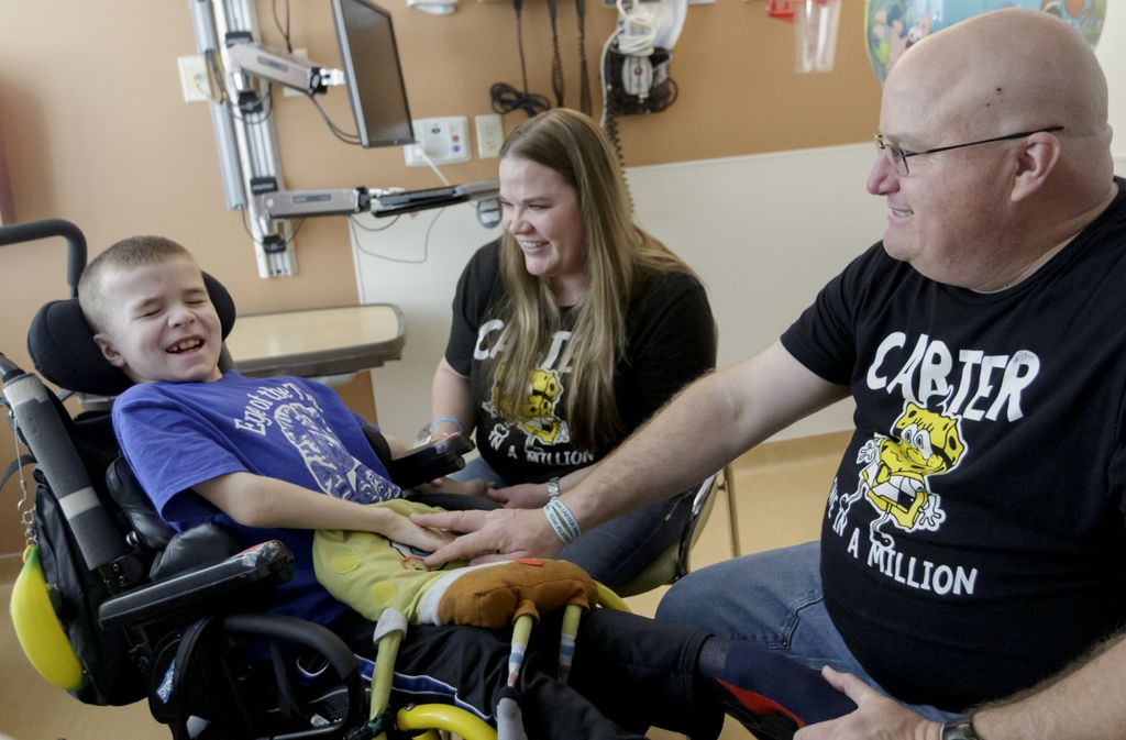 Carter, in his wheelchair, smiling with his parents.