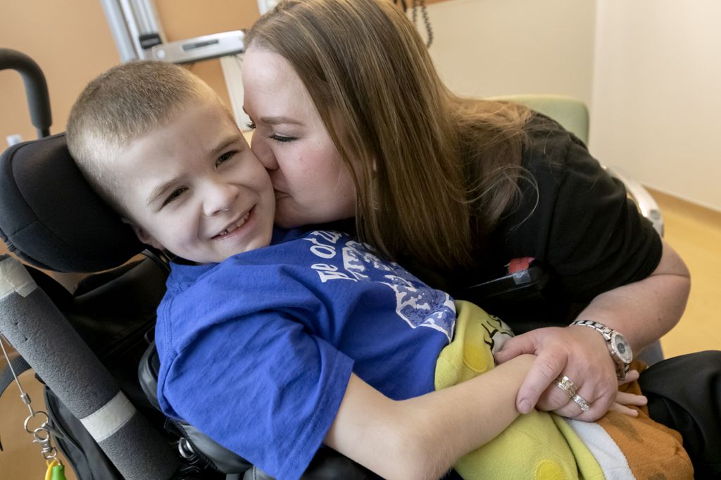 a young boy in a wheelchair, being kissed by his mother