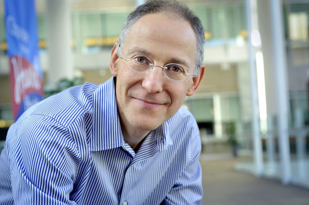 man in a blue shirt wearing glasses, pleasant smile, leaning over and looking at camera