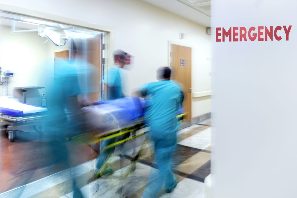 medical team wheeling patient down hall past a sign that says emergency