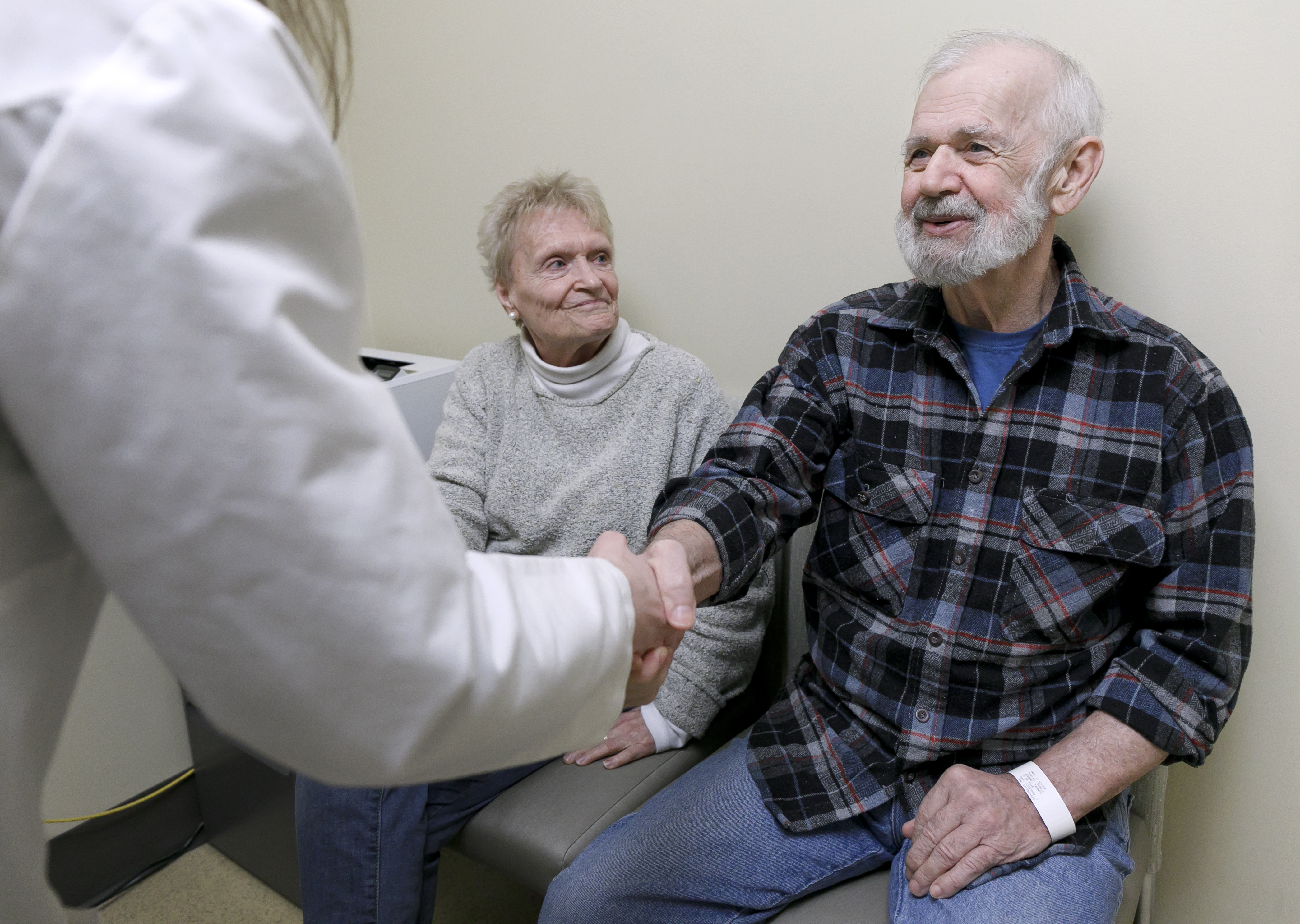 woman and man seated in doctor's office, woman looking at her husband as he shakes the hand of a doctor