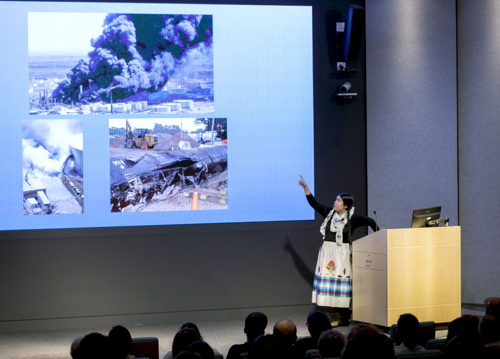 houska lecturing on stage, in front of a large screen
