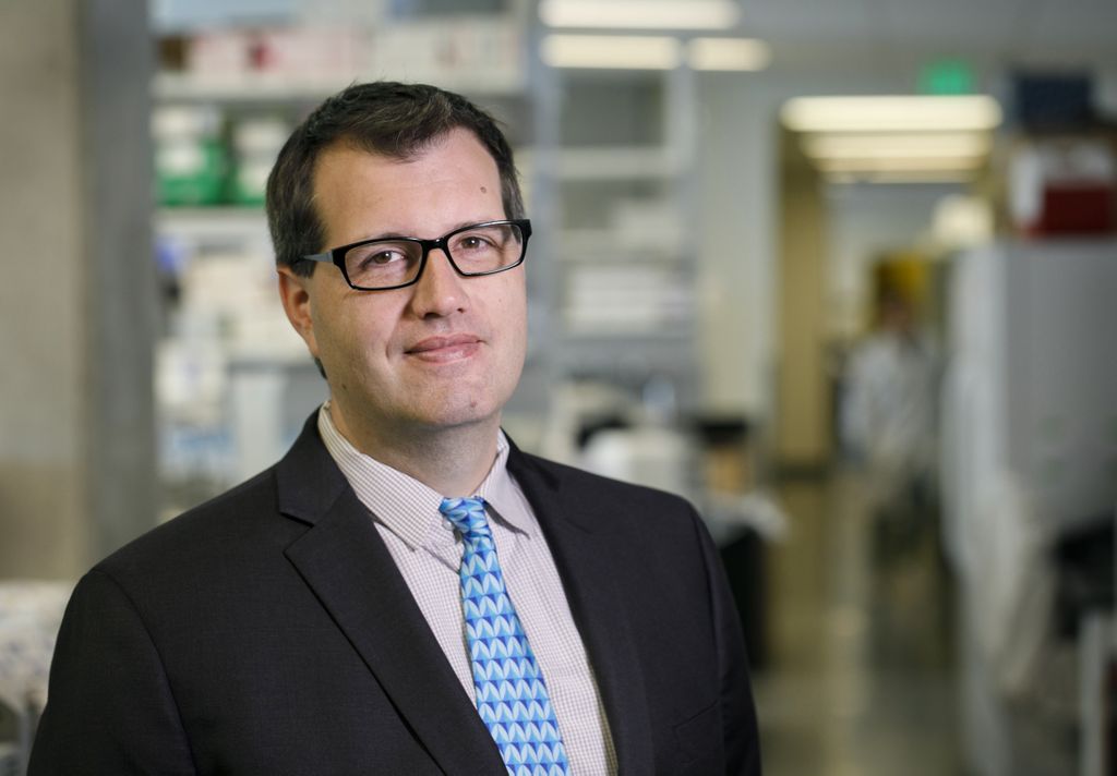 Paul Spellman, Ph.D. smiling at the camera, standing in a research lab