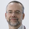 headshot of Tom Beer, M.D., F.A.C.P., a grey-haired man with glasses and a beard, wearing a white lab coat and a stethoscope