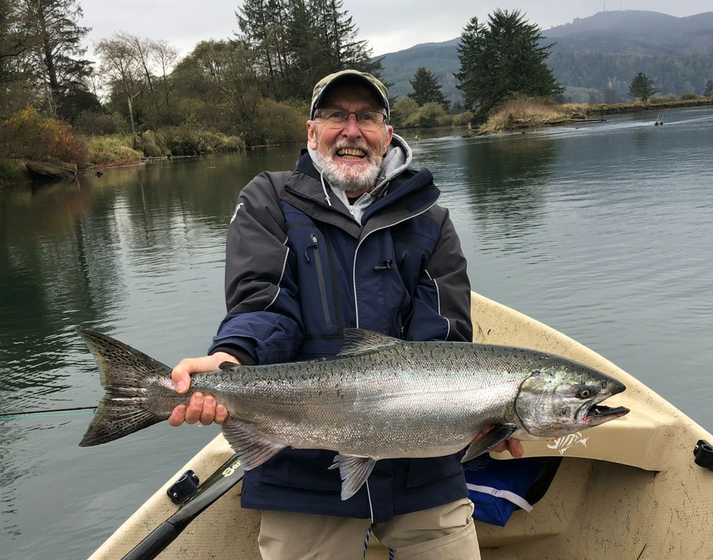 man in boat, wearing a hat and smiling, holding up a large fish horizontally, presenting it to camera