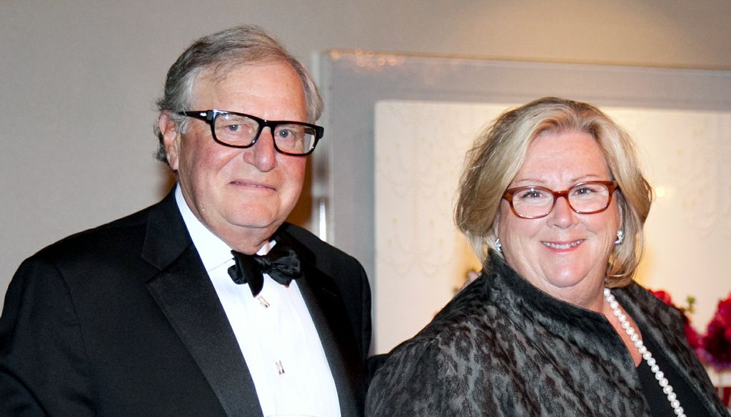 man in tuxedo, left, smiling and wearing glasses, and his wife, right, blond