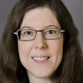 woman with long brown hair, glasses, smiling at camera 