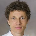 Headshot of Marcel Curlin, an adult caucasian man with curly hair and a collared shirt
