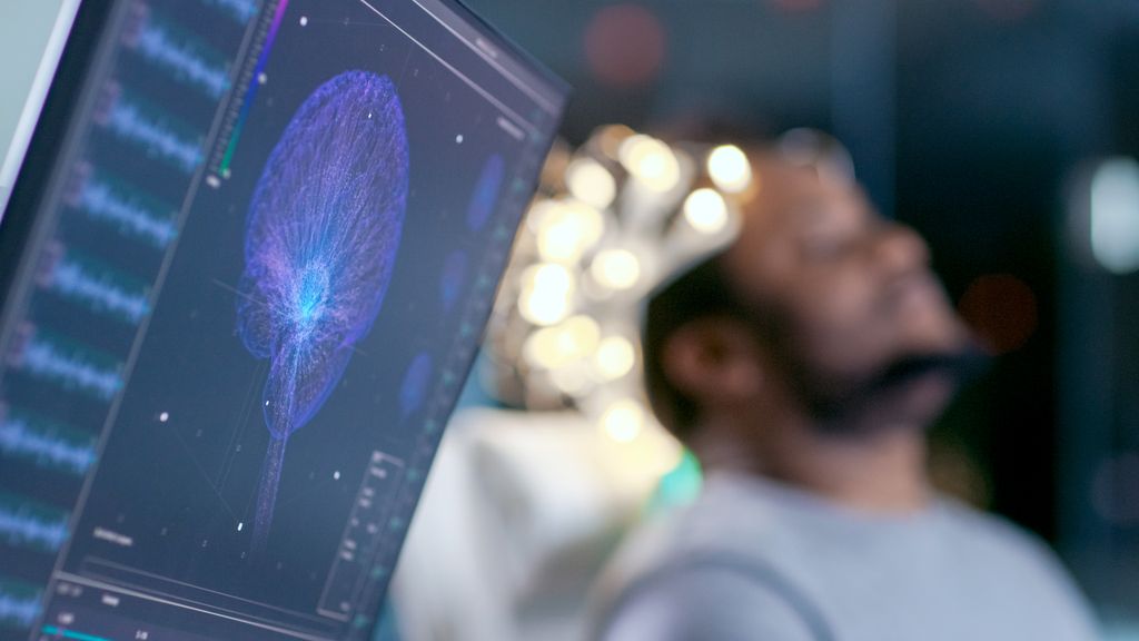 Monitors Show EEG Reading and Graphical Brain Model. In the Background Laboratory Man Wearing Brainwave Scanning Headset Sits in a Chair with Closed Eyes. In the Modern Brain Study Research Laboratory