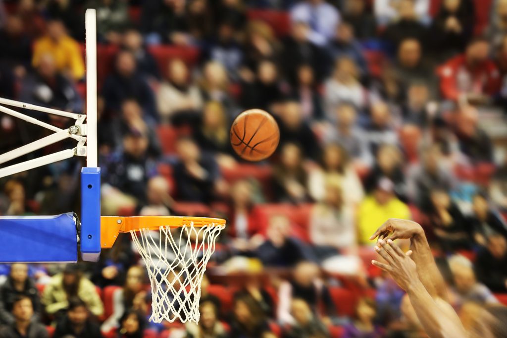 basketball being thrown toward the basket by hands in the foreground, crowd in the stands in the background
