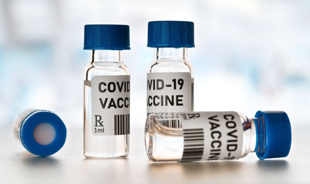 Coronavirus Covid-19 vaccine concept - small glass vials with blue caps on white table, closeup detail (own design - dummy bar code)