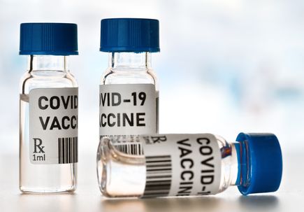 Coronavirus Covid-19 vaccine concept - small glass vials with blue caps on white table, closeup detail (own design - dummy bar code)