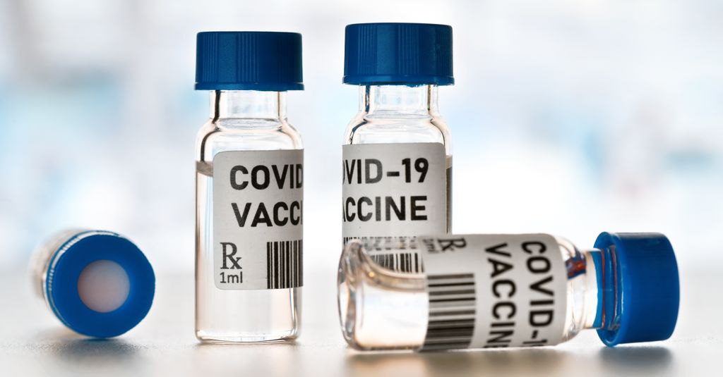 Coronavirus Covid-19 vaccine concept - small glass vials with blue caps on white table, closeup detail (own design - dummy bar code)