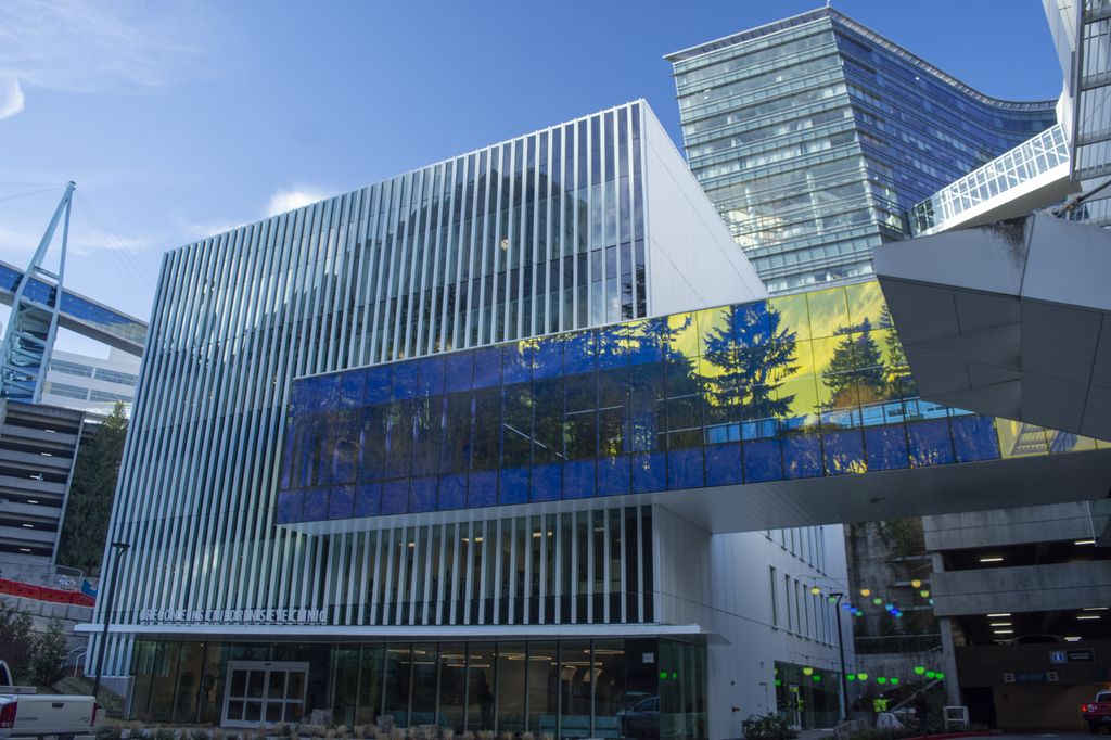 The 60,000 square-foot Elks Children's Eye Clinic building at Oregon Health & Science University's Casey Eye Institute, featureing a striking skybridge between two buildings that is adorned with color-changing glass; in the photo, the glass appears yellow with trees and clouds reflected in blue. 