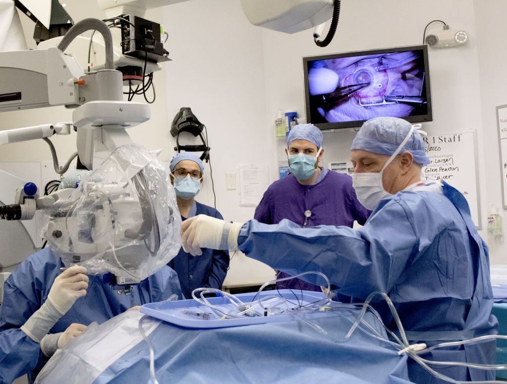 A group of surgeons in scrubs (including Dr. Pennesi, in purple) surround a patient on the operating table