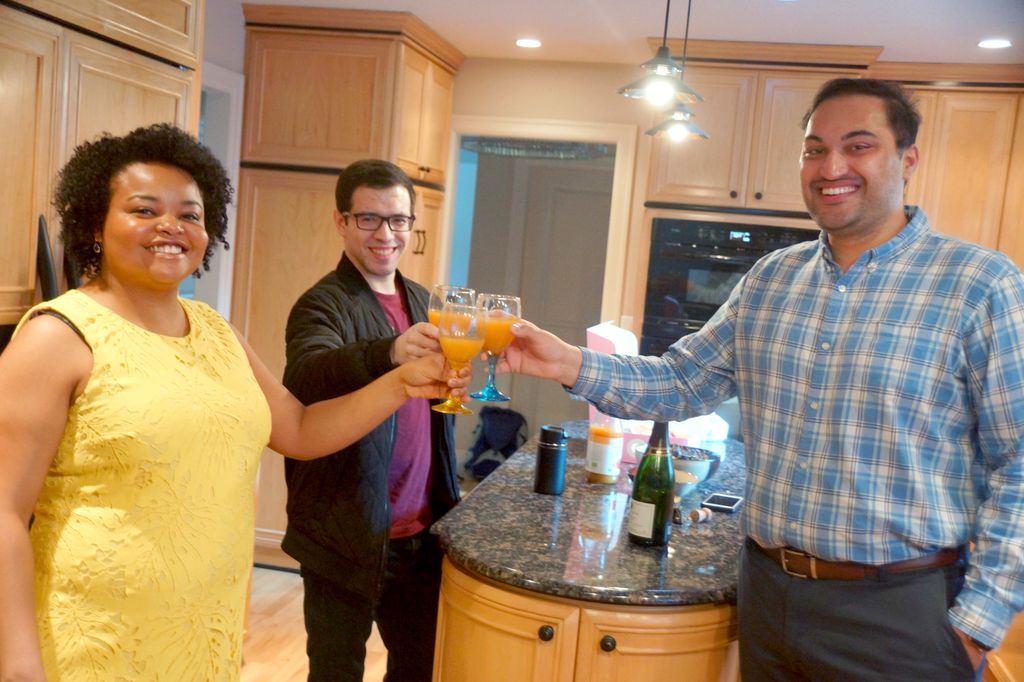 a trio of students stand facing the camera, mimosas in hand and glasses touching in the middle, raised in a toast