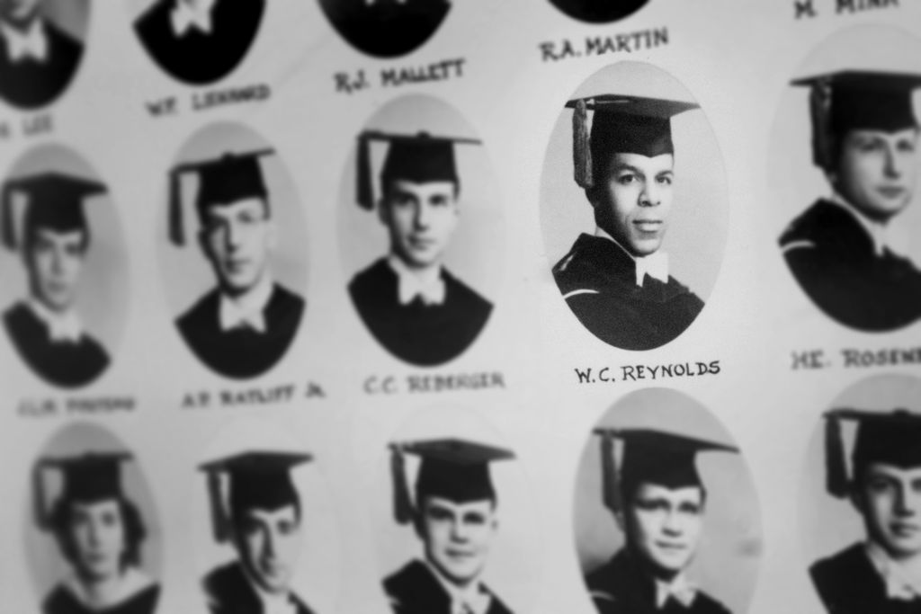 A grid of individual graduation photos highlights Walter Reynolds' image by using soft focus on the other people's photos; he is a Black man in a black graduation gown and tasseled mortar board hat