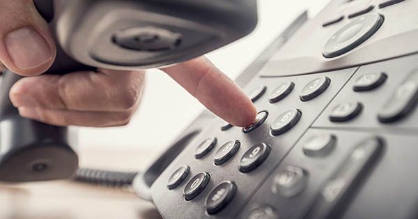 Closeup of human hand holding telephone receiver while dialing
