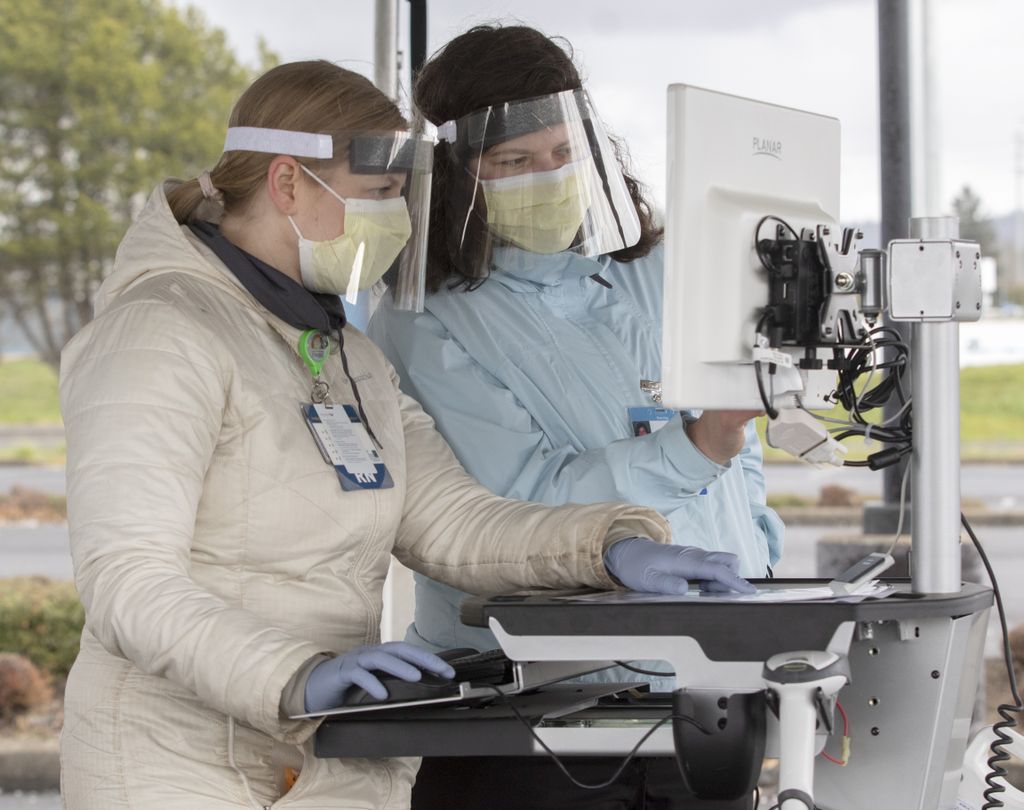 Two health care workers in masks and face shields collaborate