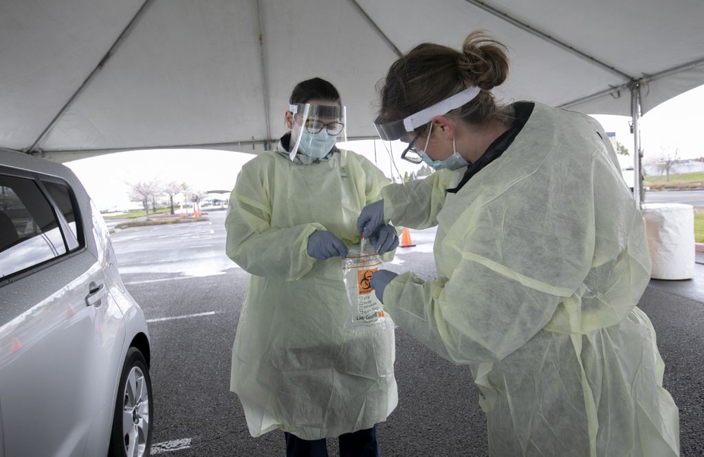 two women, dressed in protective gear, package a COVID testing sample together as they stand near a car