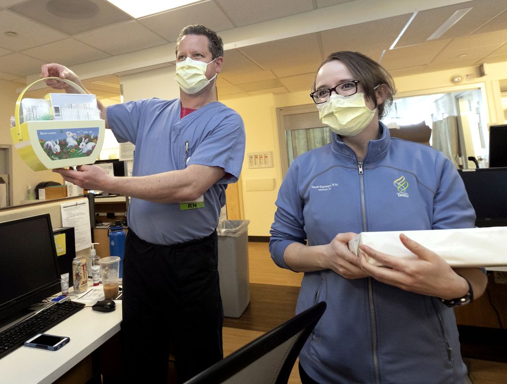 man and woman, wearing blue scrubs, man holding an easter basket full of candy, woman holding a box of chocolates