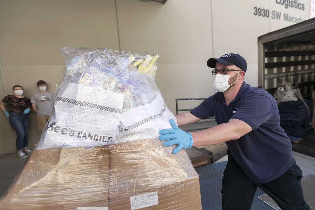 man wearing a medical mask, pushing a pallet full of See's candies up a ramp as he unloads a truck