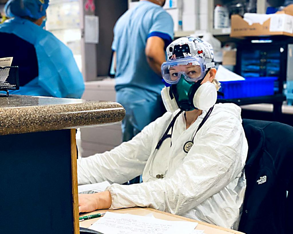 doctor in protective equipment with a large respirator on, working at a computer