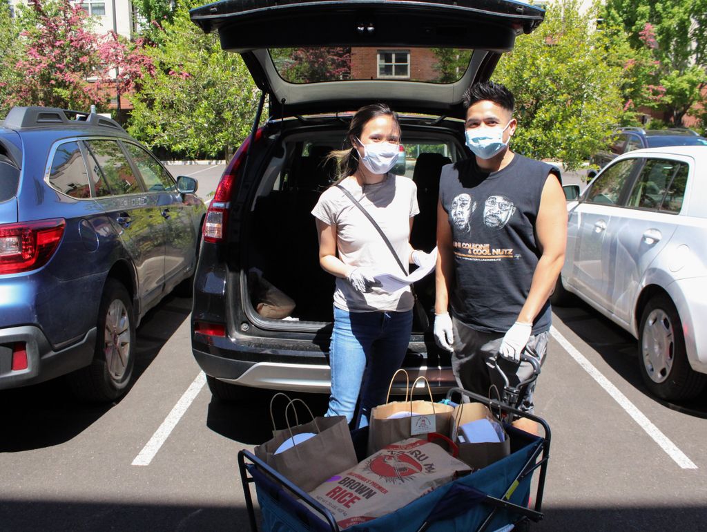two masked people, standing near the back of a vehicle with a cart