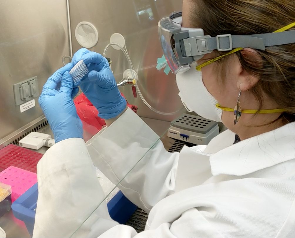 woman working at a laboratory bench with goggles on and inspecting a container