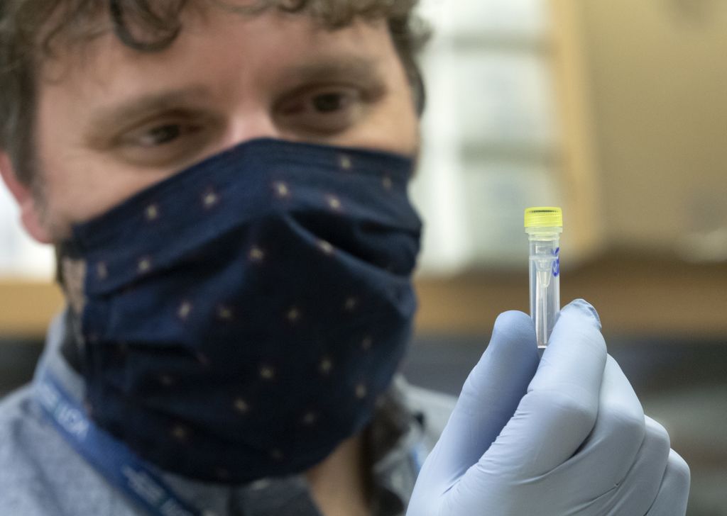 masked man, holding a vial and looking at it
