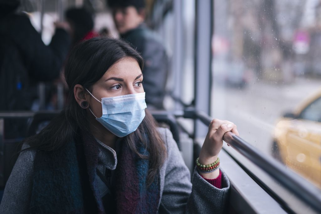 woman, wearing a mask, riding on a bus and looking out window, looking anxious