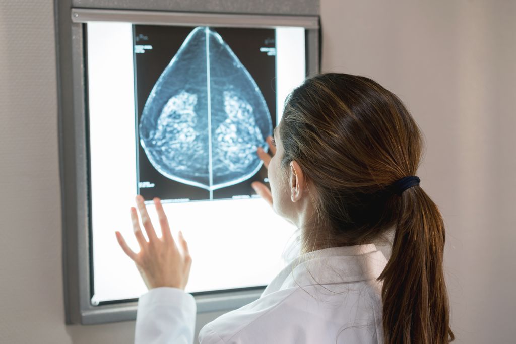 back of an unrecognizable doctor in white coat, looking at a mammogram on a white light box