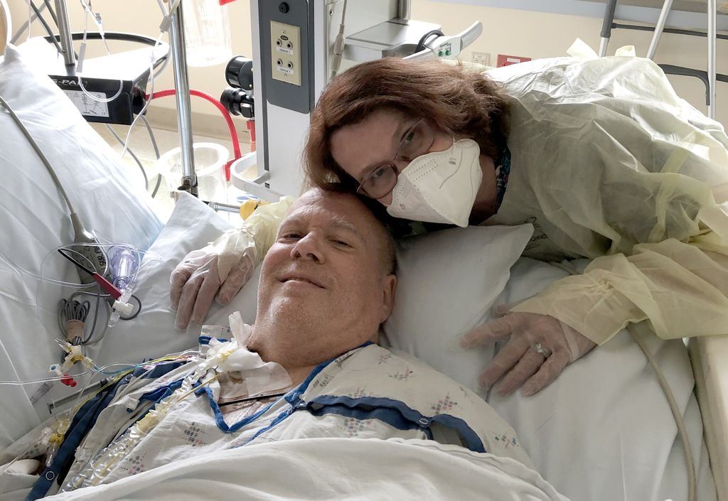 woman wearing a mask, hugging a man in a hospital bed, connected to a lot of machines and tubes