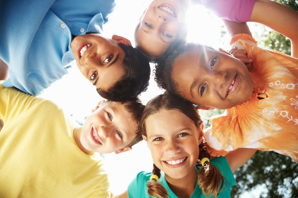 group of multiracial kids, standing in a circle looking down at camera, smiling