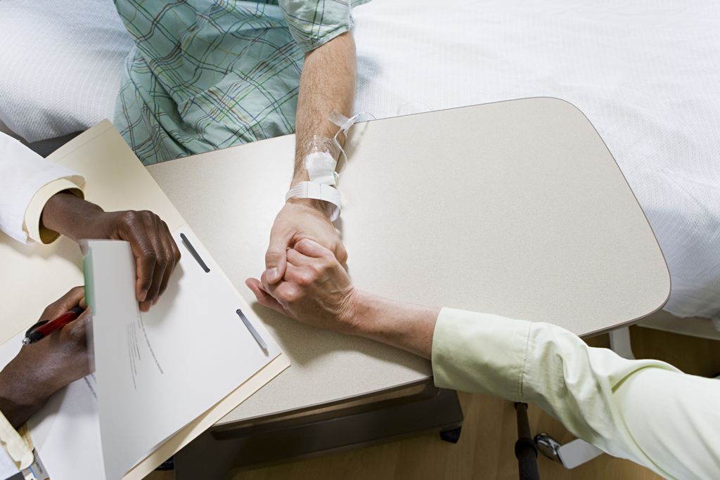 overhead image of someone in a hospital bed, holding hands with someone and talking to a doctor