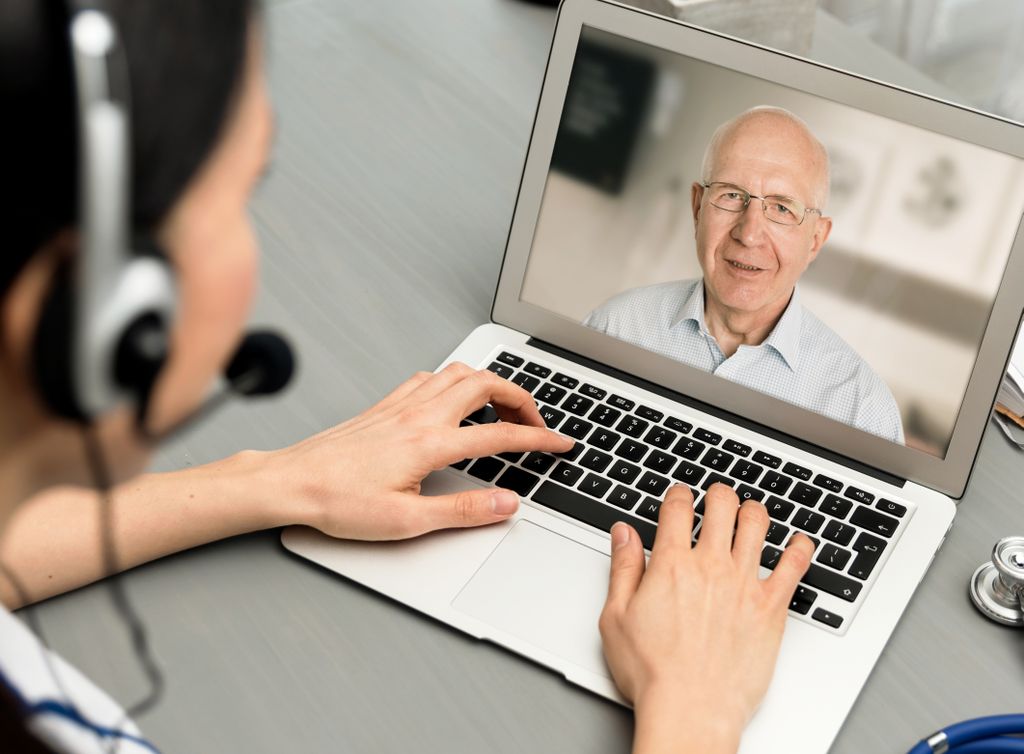 shot over the shoulder of someone wearing a headset, typing on the computer, talking to a senior on the computer