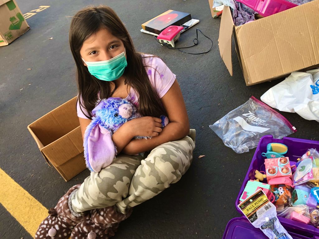 A seated, masked girl holds a purple stuffed rabbit.