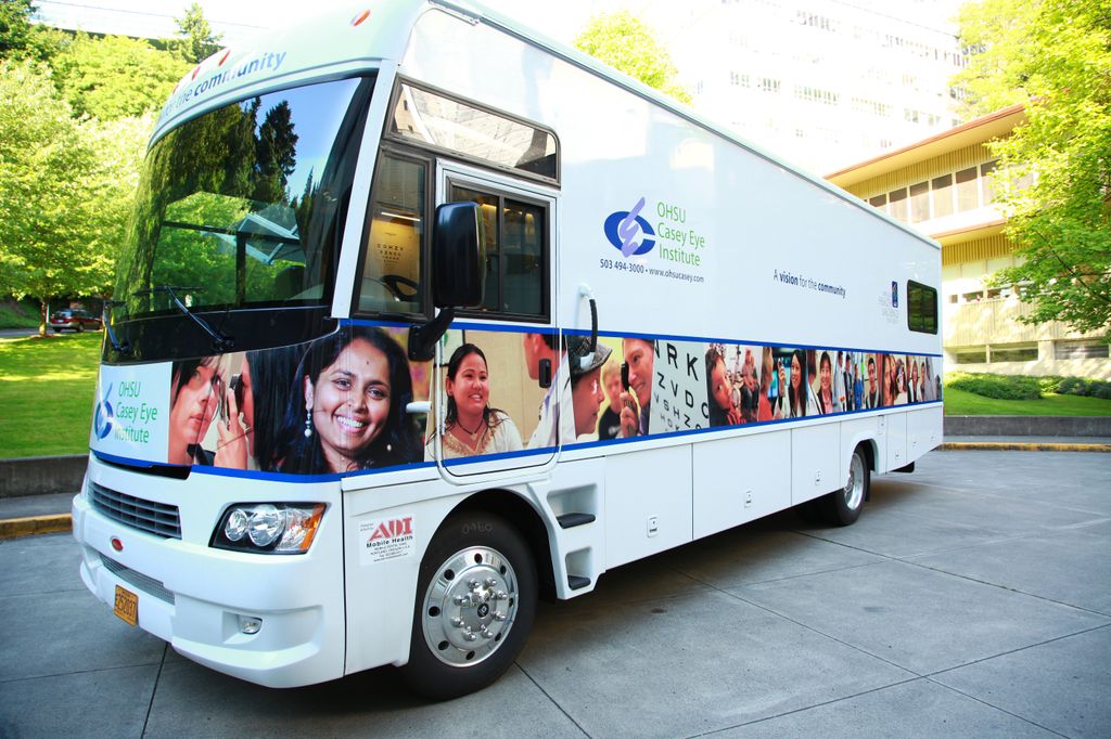 The Casey Community Outreach Program's mobile unit - a large white bus with many colorful photos of people - is shown parked, filling the frame.