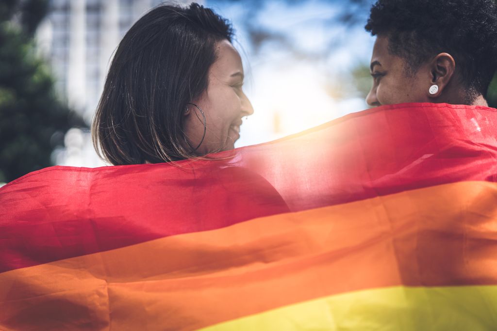 Two women's smiling faces visible above a rainbow flag,